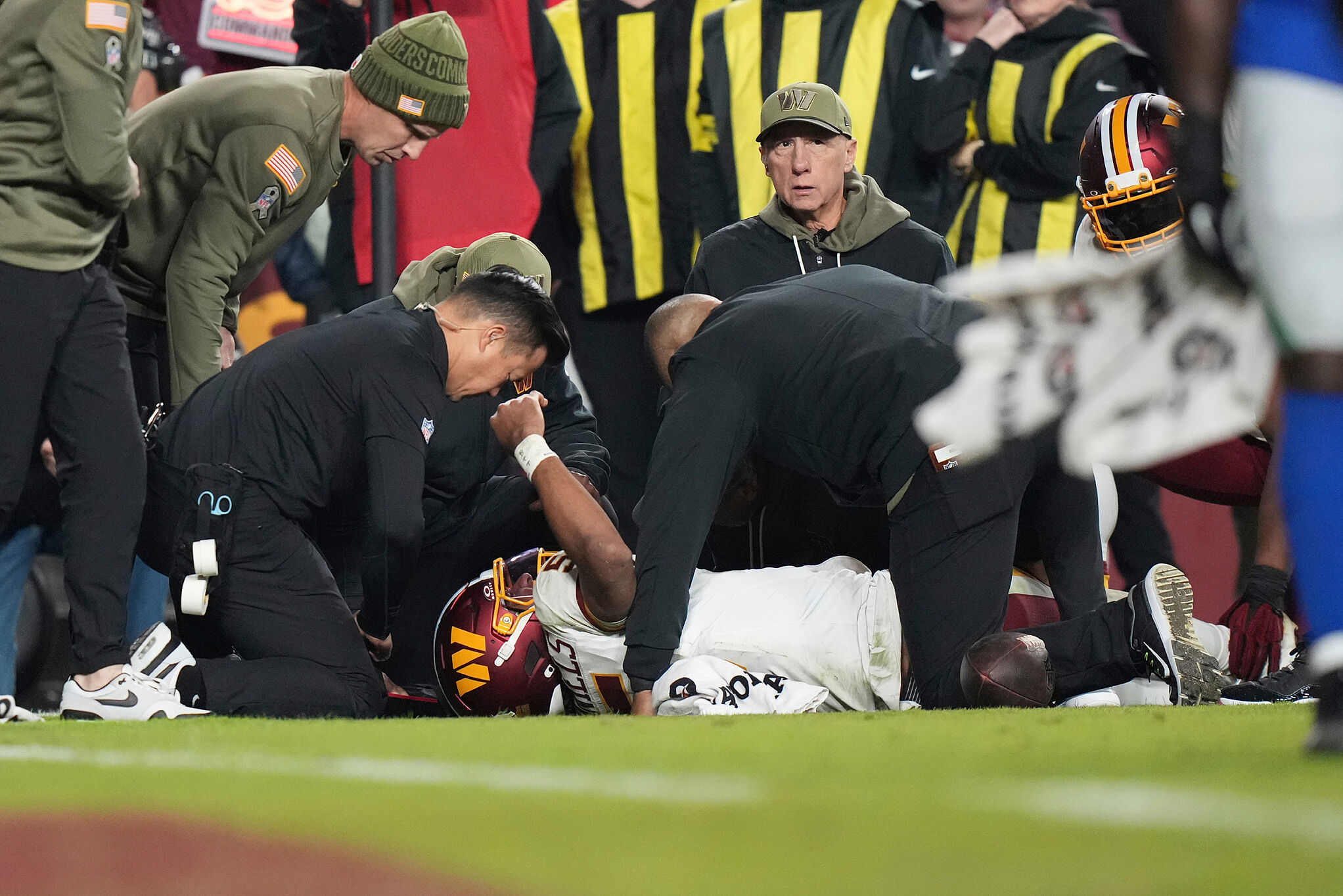 Commanders quarterback Jayden Daniels lays on the ground and is attended to by members of the Commanders medical team after injuring his arm