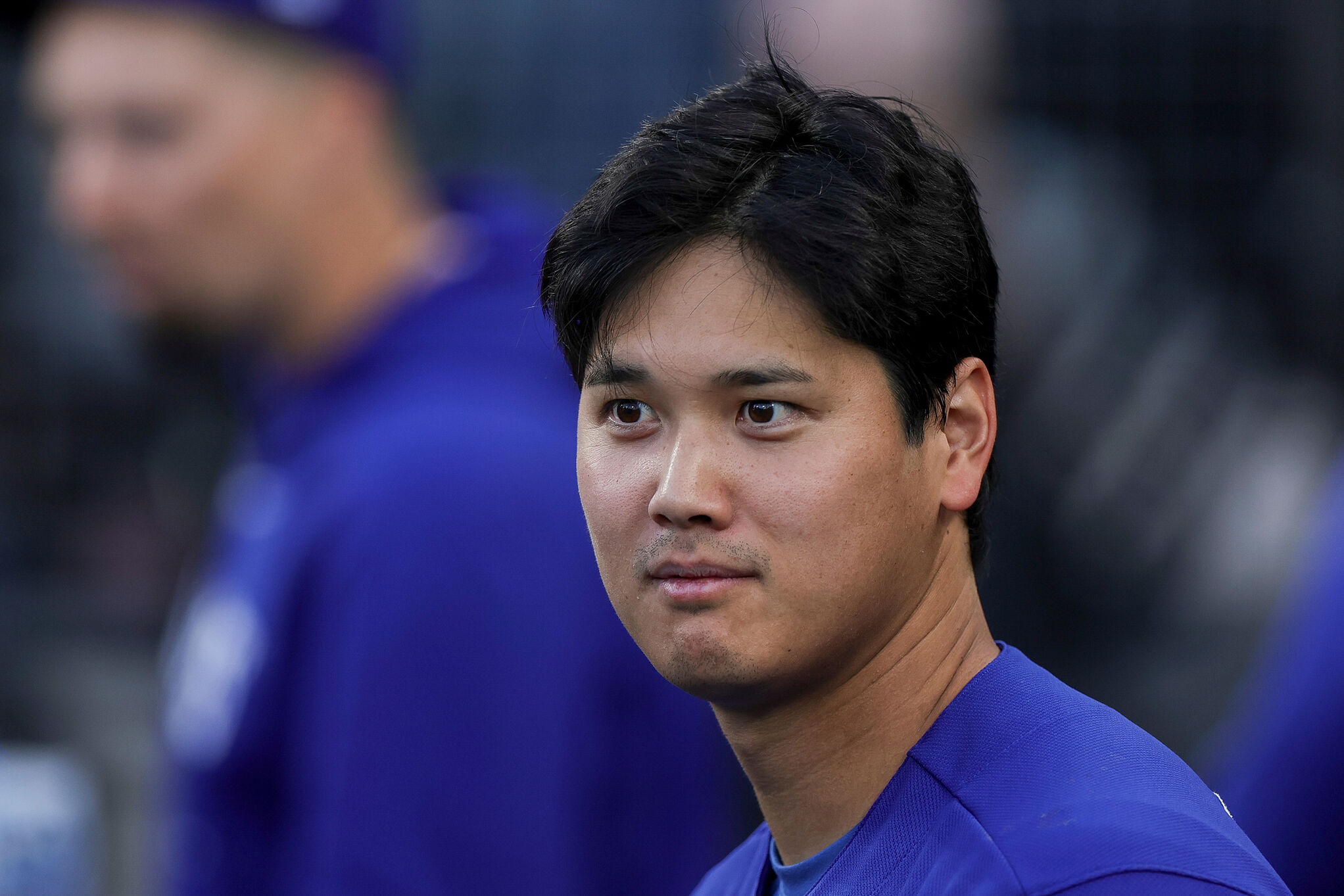 Los Angeles Dodgers' Shohei Ohtani stands in the dugout during the first inning of a spring training baseball game against the Los Angeles Angels