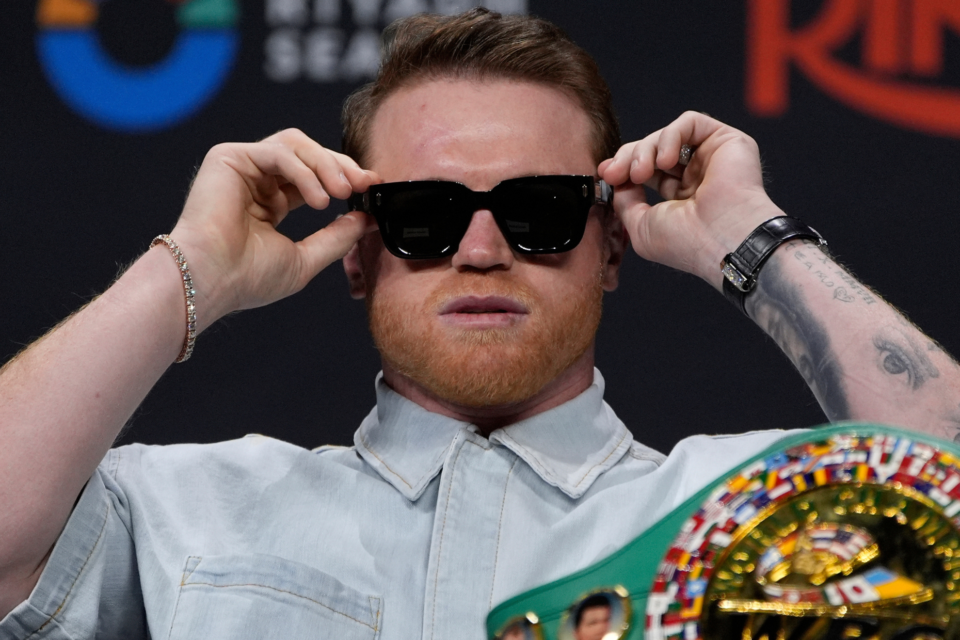 Canelo Alvarez fixes his sunglasses during a press conference alongside Terence Crawford.