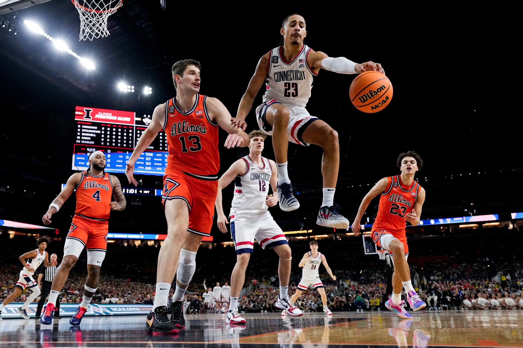 UConn forward Jayden Ross (23) reaches for the rebound as Illinois center Tomislav Ivisic (13) looks on during the first half of an NCAA college basketball tournament semifinal game